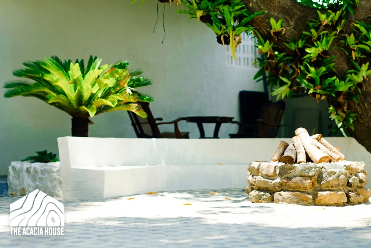 Stone fire pit with stacked logs beside white built-in seating under a large tree