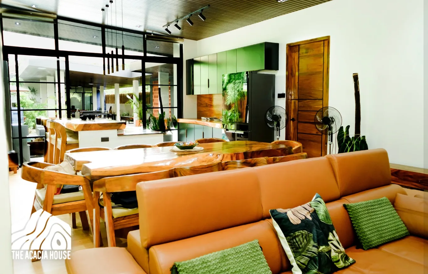 Open living and dining area with a live-edge wooden table, leather sofa and green kitchen cabinets