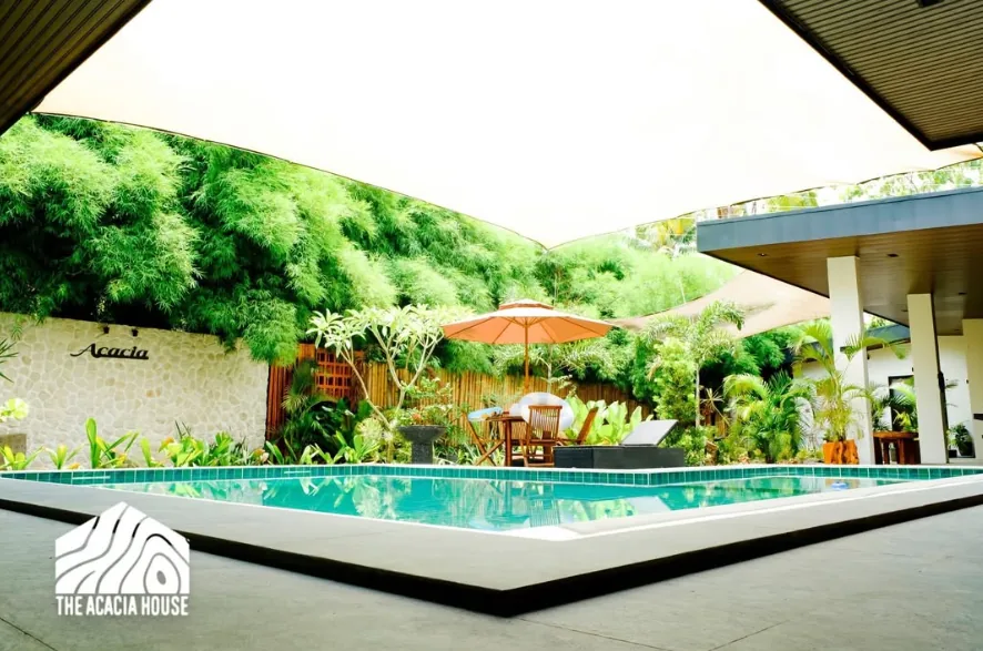 The private pool at The Acacia House under a white shade sail, with the Acacia stone wall and tropical garden behind