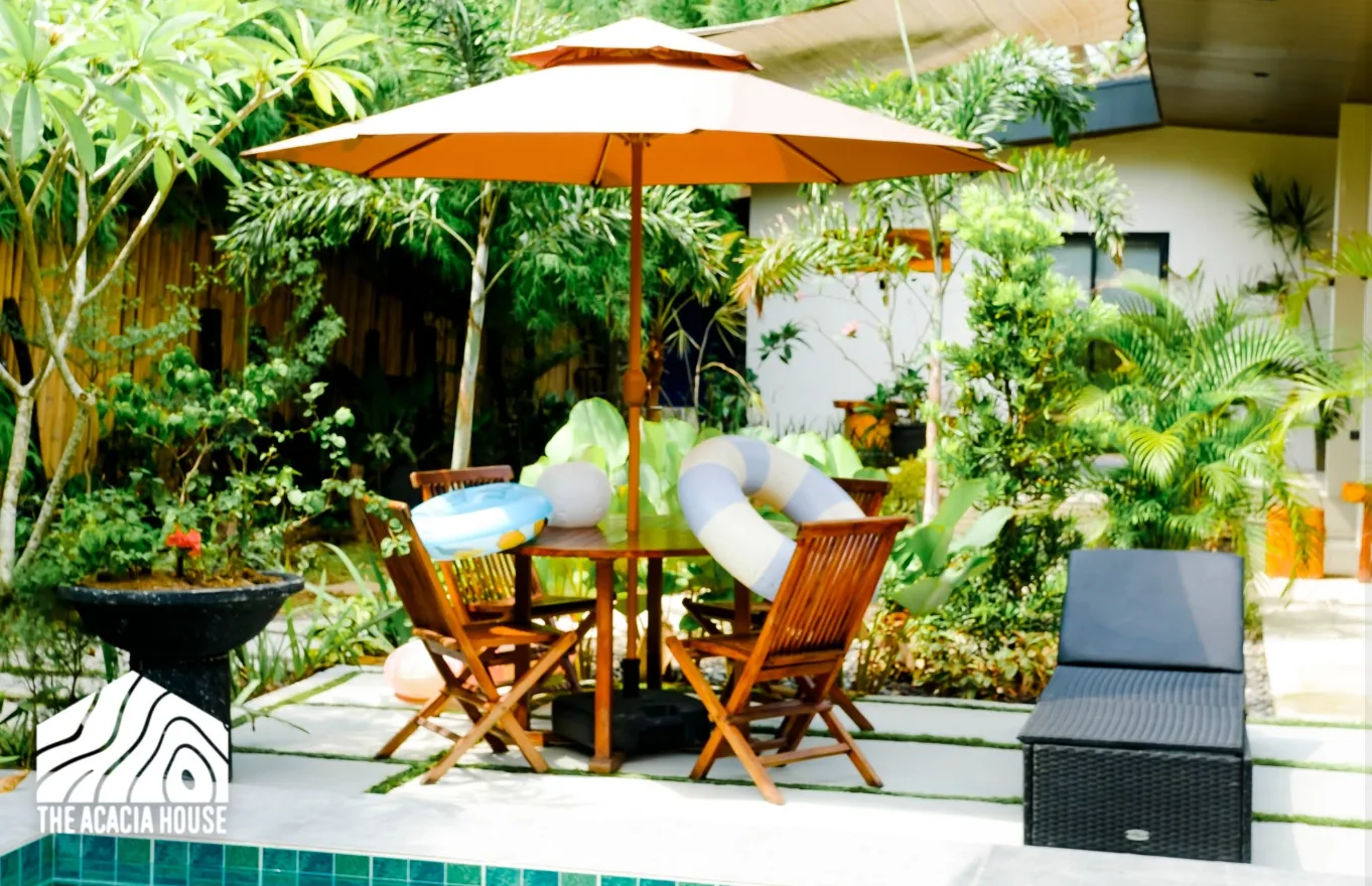 Poolside table and folding chairs under an orange umbrella with pool floats